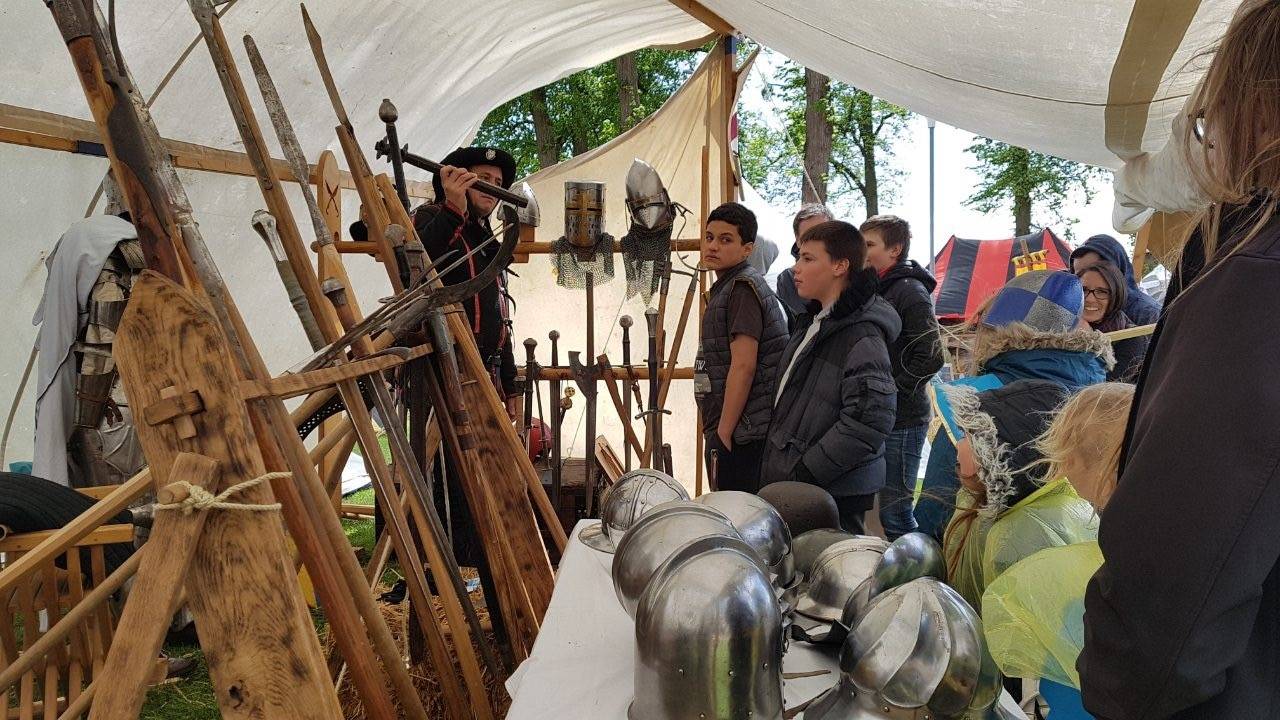 Présentation d'armes et de casques sous une tente, devant un groupe d'adultes