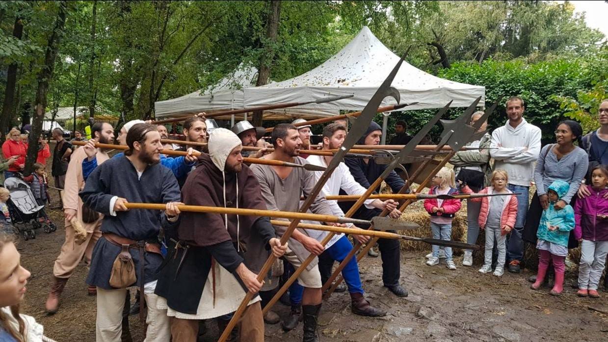 Une ligne de piquiers en costume tend ses piques devant un public de familles